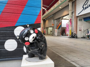 八代本町アーケードの路地裏で見つけた面白いフォトスポット。カラフルな壁画の前で悪だくみポーズをとるお茶目なくまモン。