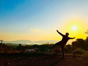 天草の山間から海を望む夕焼け。地平線に沈む太陽に向かって両手を広げ、感動を表現する人物。