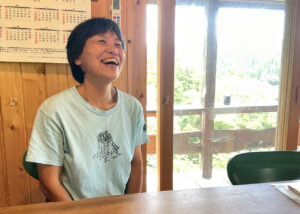 事務所のテラスから見える緑を背景に、インタビューに答える國武信子さんの朗らかな笑顔。