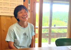 事務所のテラスから見える緑を背景に、インタビューに答える國武信子さんの朗らかな笑顔。