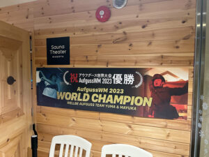 サウナシウェルビー栄店の木製の壁に掲げられた「祝 アウフグース世界大会 優勝 AufgussWM 2023 WORLD CHAMPION」の横断幕。