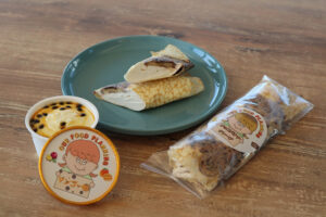 OUR FOOD PLANNINGが手掛けるスイーツ。木のテーブルに置かれたチョコバナナクレープとマンゴープリン。カットされたクレープの断面から、たっぷりのクリームが見える。