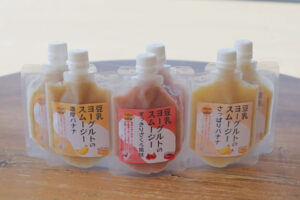 豆乳スムージー「スグルト」の商品ラインナップ。濃厚バナナ、すっきりざくろ風味、さっぱりバナナの3種類が並んでおり、手軽に栄養補給できるパウチ容器が特徴。