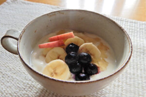 手作り風のヨーグルトボウルのアイキャッチ画像。陶器の器に盛られたヨーグルトに、バナナ、ブルーベリー、りんごのスライスがトッピングされ、はちみつがかかっている。健康的で美味しい朝食のイメージ。